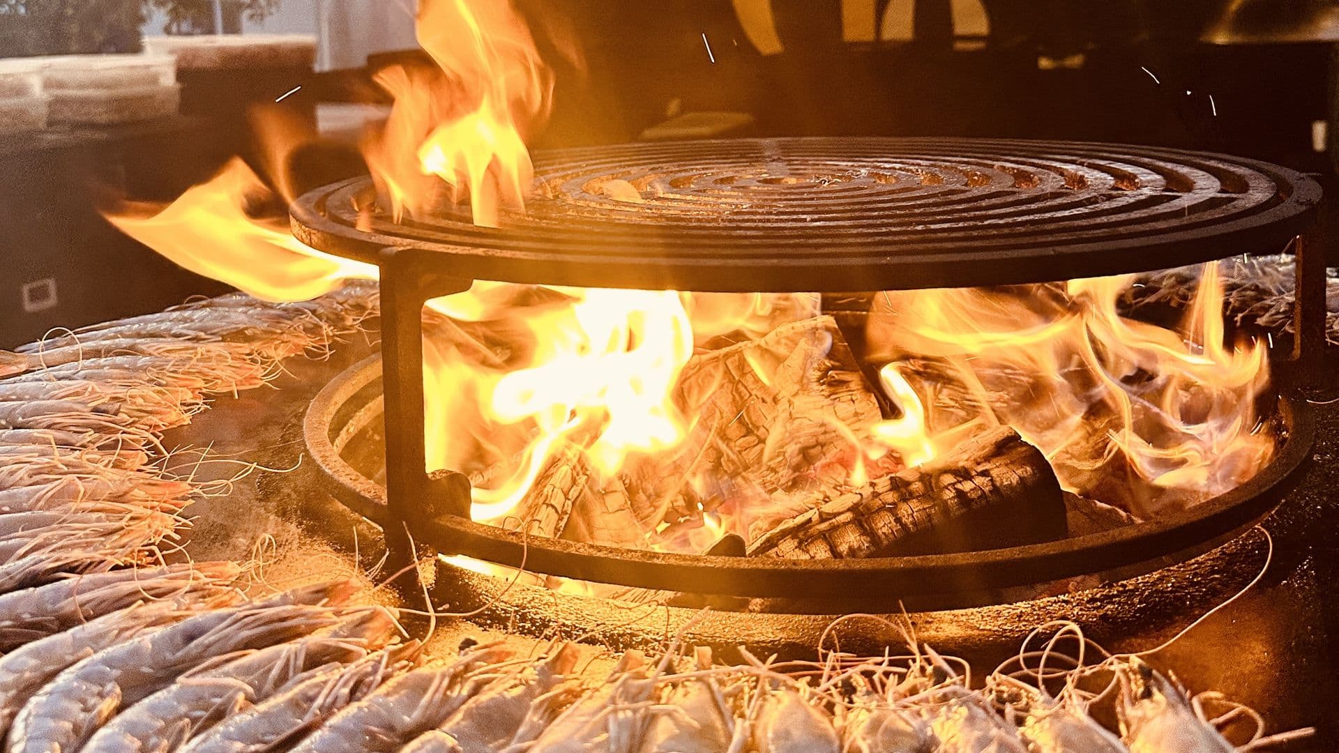 Gambas en persillade disposées autour d'un brasero Grasgueule en flammes, à la tombée du jour