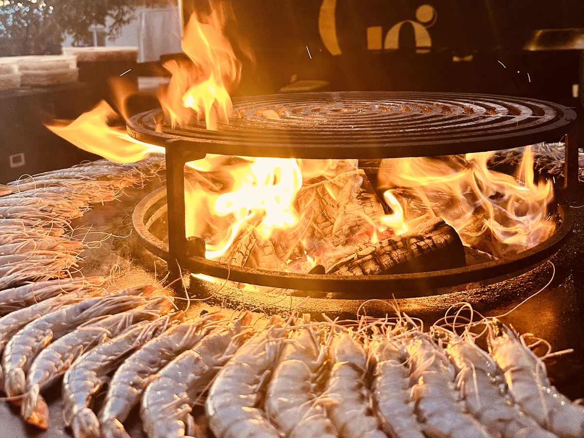 Gambas en persillade disposées autour d'un brasero Grasgueule en flammes, à la tombée du jour